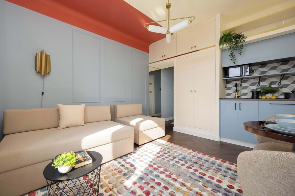 A wider view of the living area showing a couch, a small table with decor, and an open connection to a kitchenette space. The ceiling has a bold orange accent.