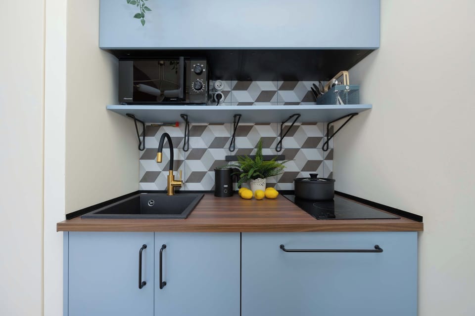 A compact kitchenette area with blue cabinets and a black countertop. Open shelving displays dishes and small decorative items.