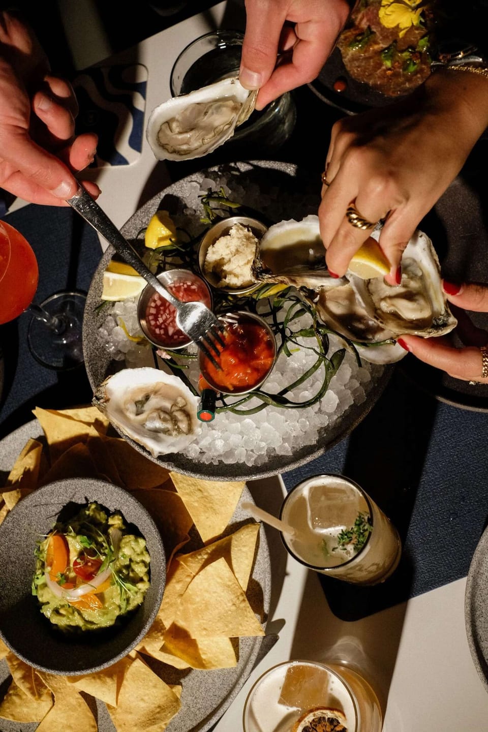 Hands reaching for oysters on ice with sauces and citrus