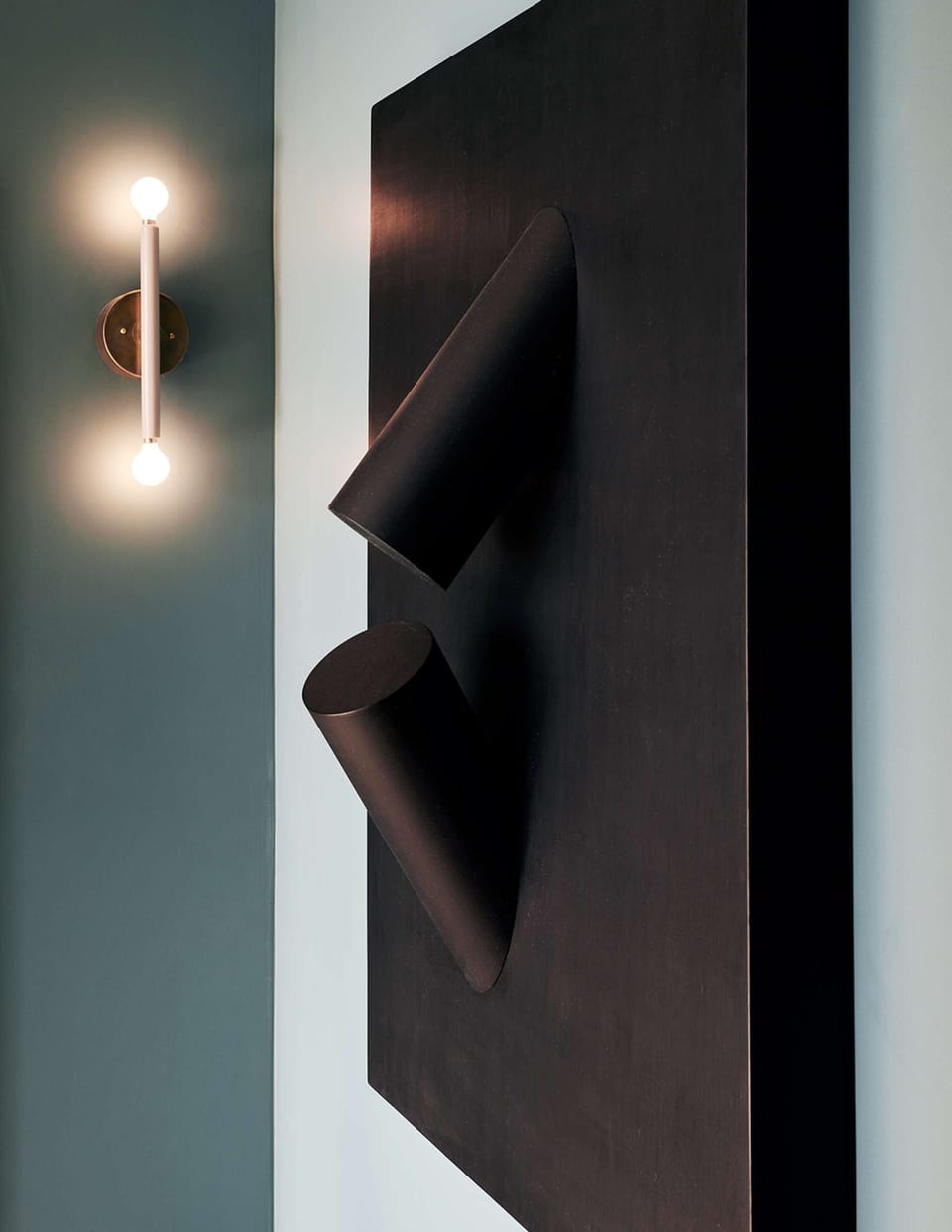 Sculptural black wall piece paired with brass light on muted wall