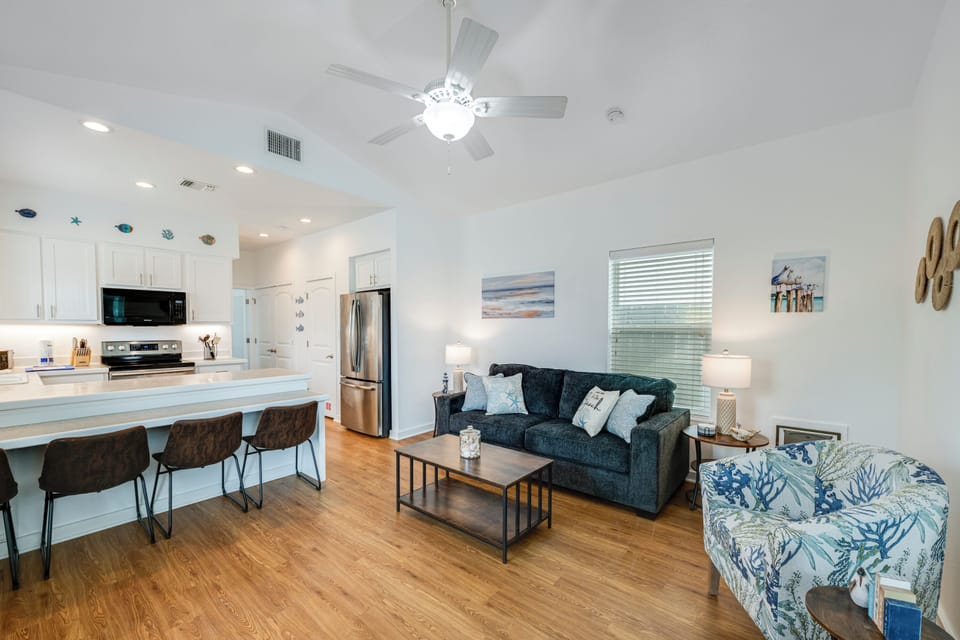 Relax in your bright, modern living space featuring coastal decor, a fully equipped kitchen, and cozy seating perfect for unwinding after beach adventures.