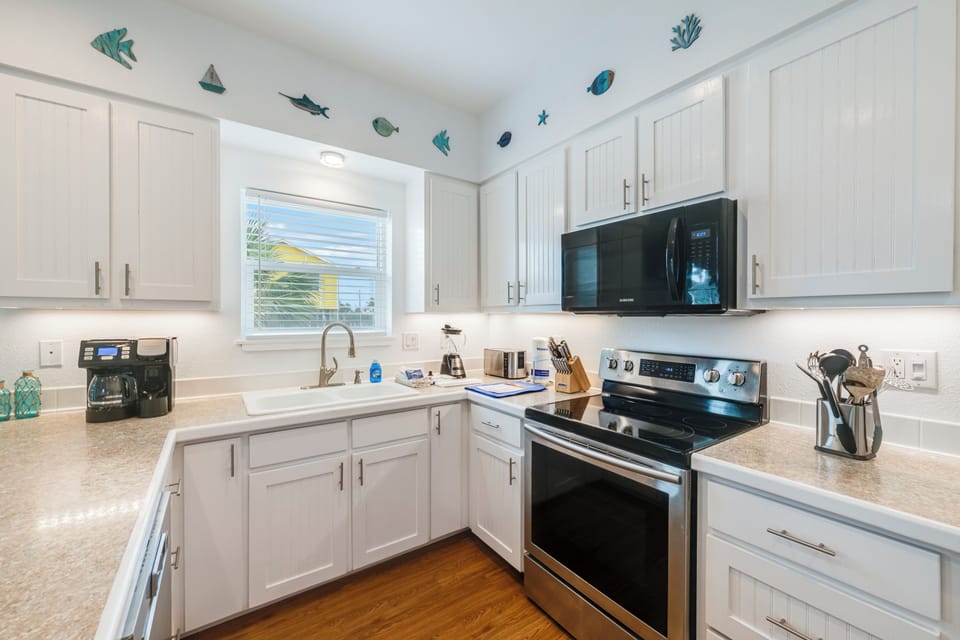 Your fully equipped kitchen sparkles with white cabinets, granite counters, and stainless appliances—perfect for preparing seaside meals beneath whimsical fish decor.