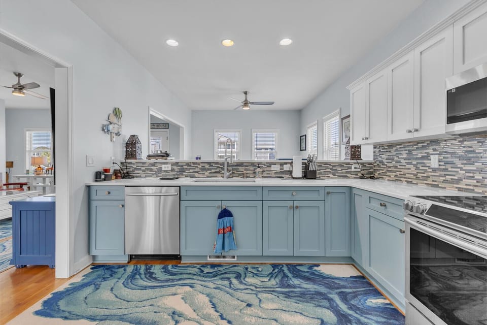 You'll love cooking in this stunning coastal kitchen with sea-inspired blue cabinets, granite counters, and ocean wave rug underfoot.