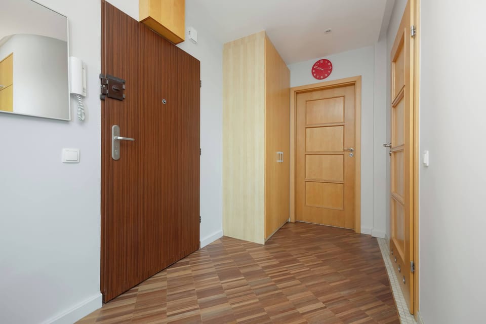 An entryway with a dark wood front door and an intercom, decorated in a subdued color scheme.