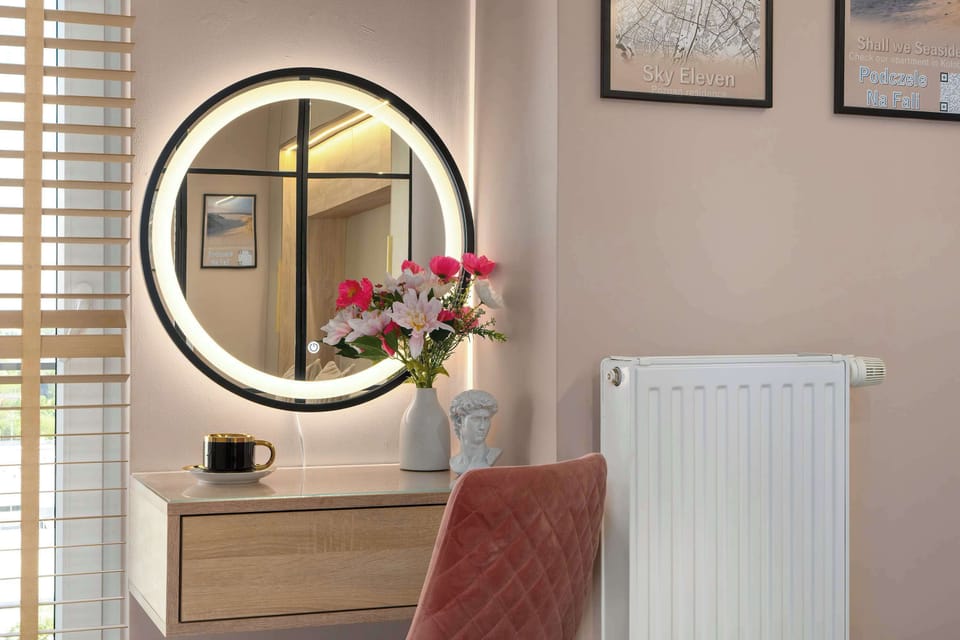 A dedicated vanity corner offers a circular illuminated mirror above a sleek wooden desk with a plush pink chair.