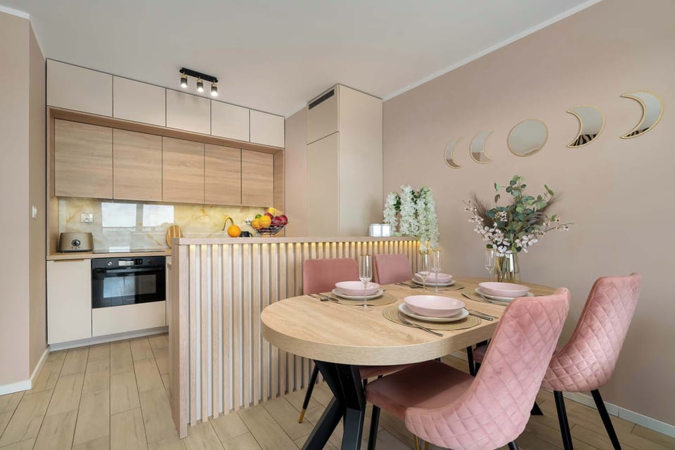 A dining area is furnished with a wooden table, soft pink velvet chairs, and a decorative wooden slatted room divider.