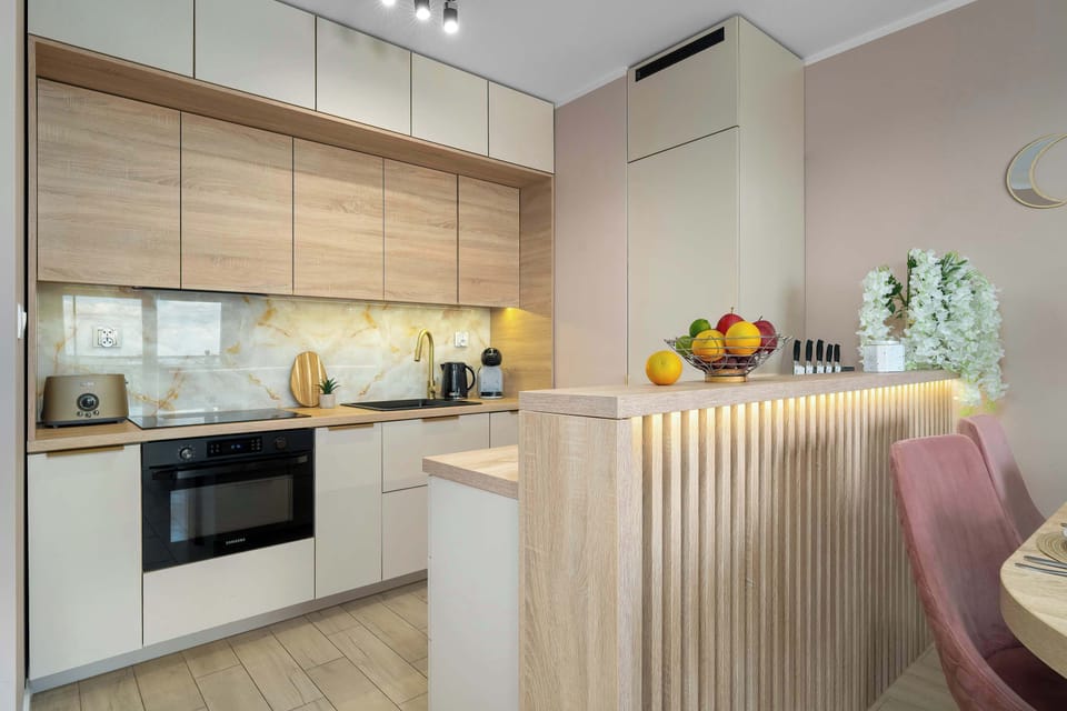 A modern kitchenette view reveals sleek white countertops, integrated appliances, and warm under-cabinet LED strip lighting.