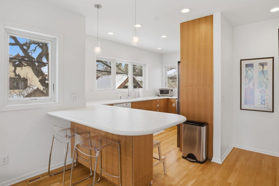 Your sleek modern kitchen features warm wood cabinetry, bright white countertops, and large windows that flood the space with natural light.