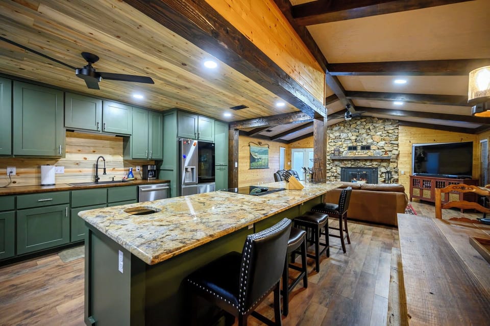 Your mountain kitchen combines rustic charm with modern convenience—granite counters, green cabinets, and exposed beams create the perfect gathering space for your getaway meals.