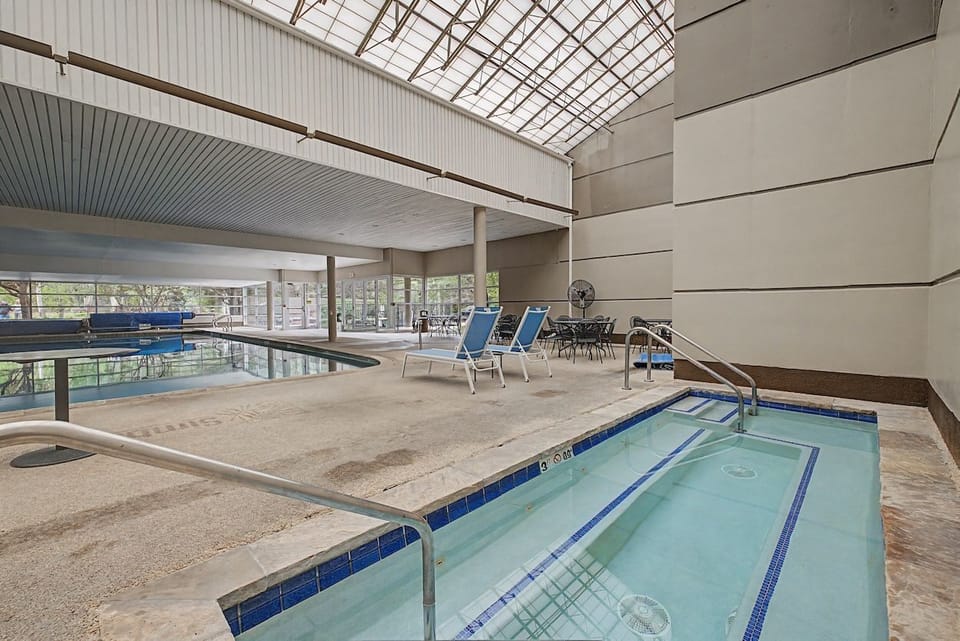 Indoor swimming pool and hot tub area illuminated by natural skylights.