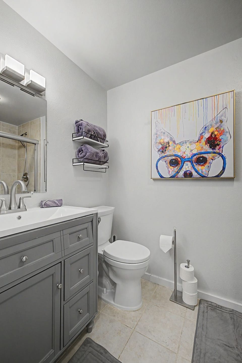 Bathroom featuring a gray vanity, white toilet, and colorful framed wall art.