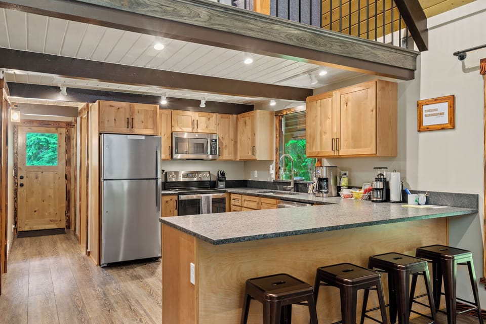 Fully equipped kitchen with stainless steel appliances, wooden cabinetry, and breakfast bar seating