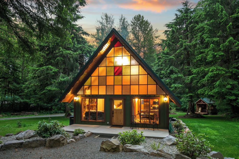 A-frame cabin glowing at dusk with iconic stained glass windows and manicured forest setting