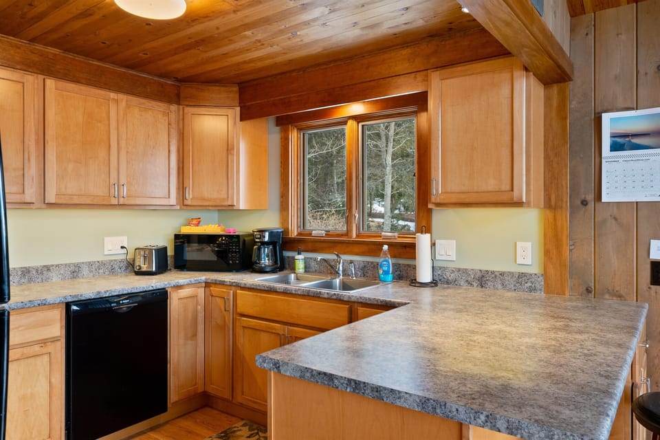 Traditional finishes and harbor-bound views. Our kitchen features natural wood cabinetry and a view into the wooded landscape toward the water. Stocked with essential spices and coffee, it’s a ready-to-use space for your Quiet Side stay.