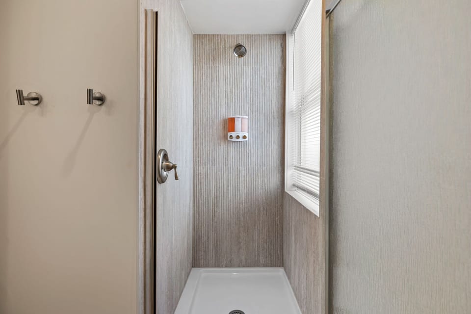 Walk-in shower with a textured surround, glass enclosure, window, and wall-mounted dispensers.