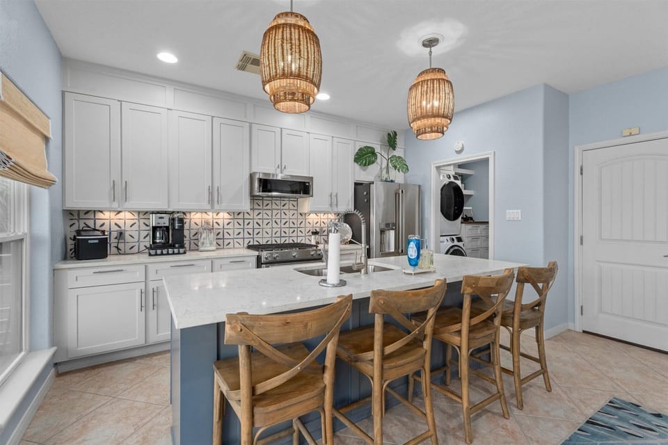 Modern coastal kitchen with large island, bar seating, pendant lighting, and stainless steel appliances.