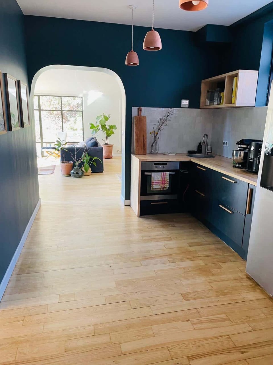 Cuisine aménagée avec murs bleu nuit, arche ouverte sur le séjour et vue jardin