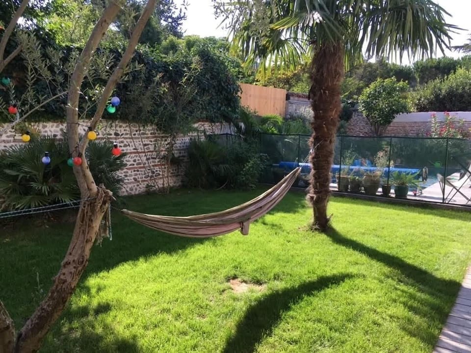 Jardin arboré avec hamac entre les arbres et pelouse, piscine en arrière-plan