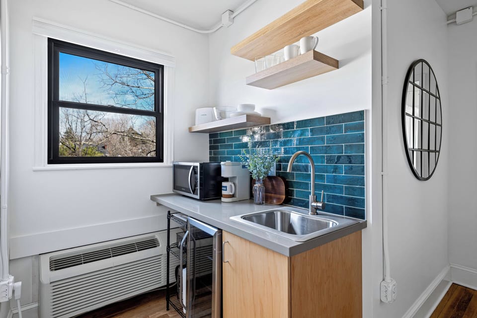 Bright kitchenette with modern finishes, featuring a mini fridge, microwave, coffee setup, and everything needed for easy, convenient meals.