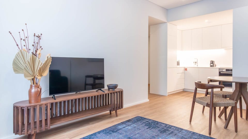 Bright and airy living space featuring a modern TV setup, beautifully paired with a sleek wooden console and minimalist décor. The open kitchen is just steps away. #CozyLiving #ModernDesign