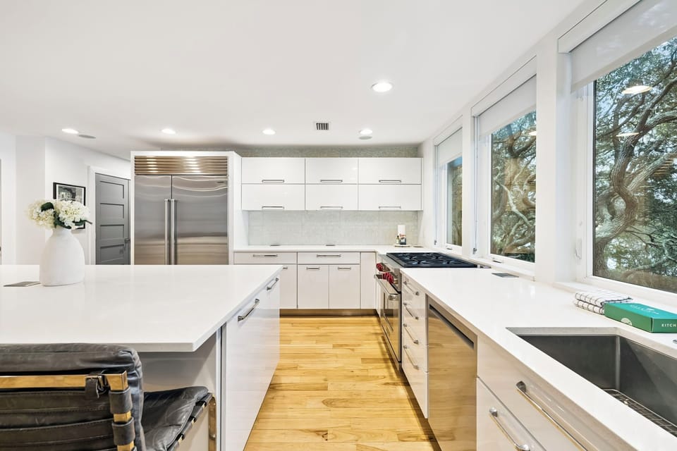 Your modern kitchen awaits with sleek white counters, stainless appliances, and abundant natural light streaming through garden-view windows.