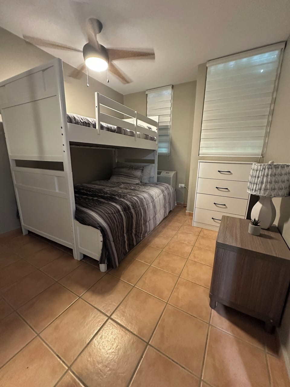 Efficient bedroom with white bunk beds, ample storage, and cool tiled flooring.