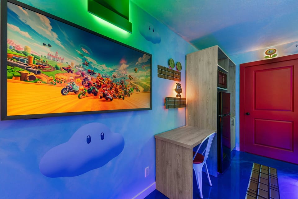 A gaming-themed room featuring a large screen, colorful wall art, and a compact desk area.