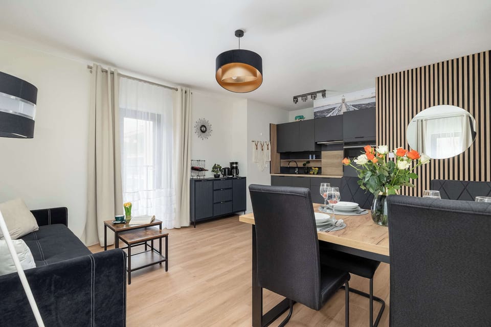 The perspective from the living area looks toward the kitchen, revealing a cohesive open floor plan. A black chandelier hangs from the ceiling, adding a touch of industrial style to the room.