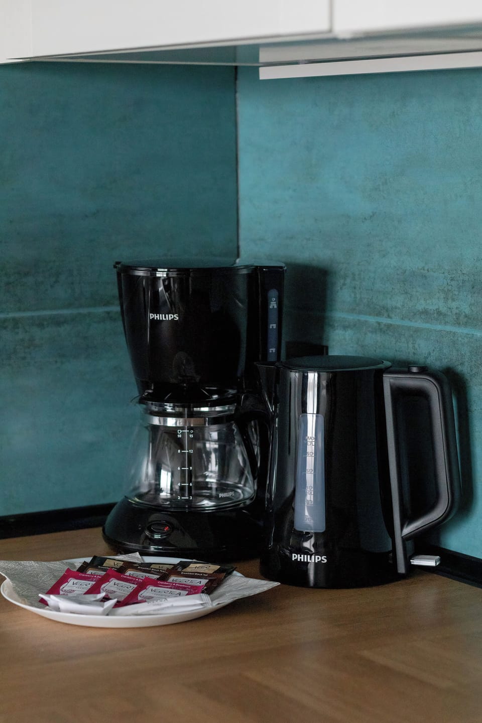 A close-up of a coffee machine in the kitchen highlights convenience for guests. The teal backsplash and wooden countertop create a stylish combination. Everything looks clean and ready to use.