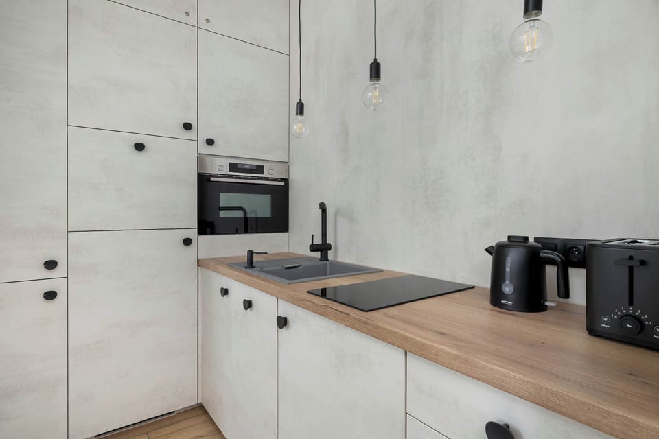 A section of the kitchenette with a dark sink and a modern cooktop, integrated into a light-colored countertop with a wood grain finish. Tall cabinetry provides plenty of storage space.