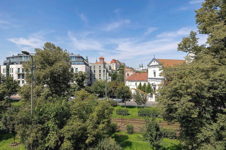 A view of a dense canopy of trees and neighboring buildings in the distance, suggesting the proximity of parkland. The picturesque panorama of the area promises a quiet and peaceful stay.