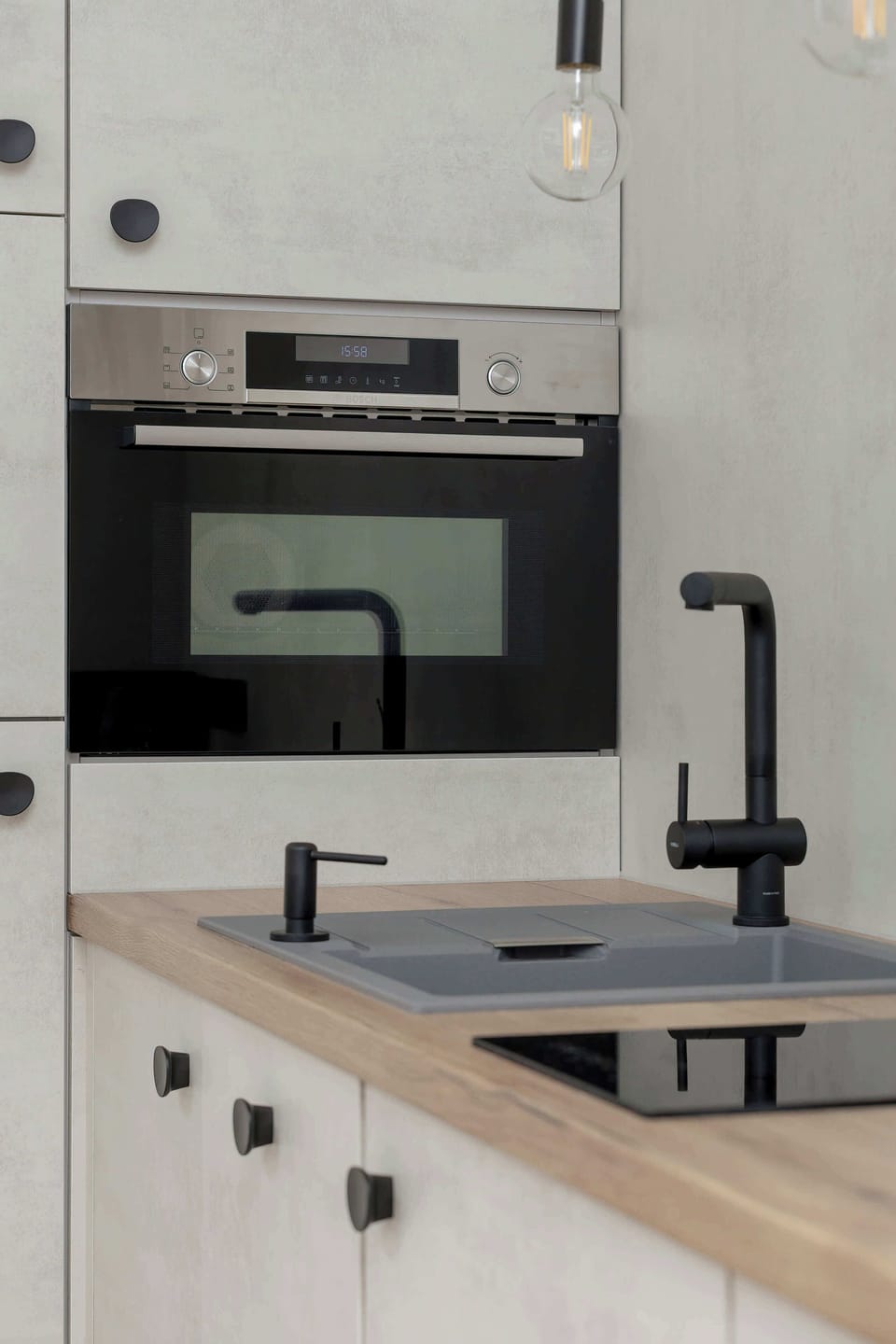 A vertical view of a cabinet with a built-in 2in1 oven, highlighting the clean lines and high-quality finish of the furniture. The contrast between the white cabinet fronts and the black appliances adds dynamism to the interior.
