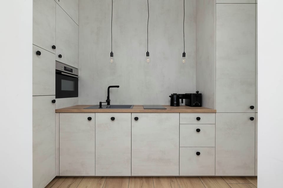 Minimalist white kitchenette cabinets with black fixtures, showcasing a modern design. Smooth fronts emphasize the room’s clean lines and aesthetic appeal.