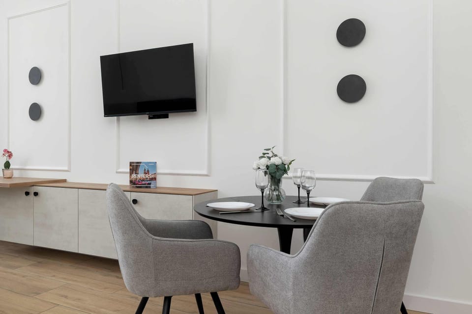 An entertainment area with a TV mounted on the wall above a long, white dresser that stretches the entire length of the room. Black, round details on the wall create a modern decorative accent.