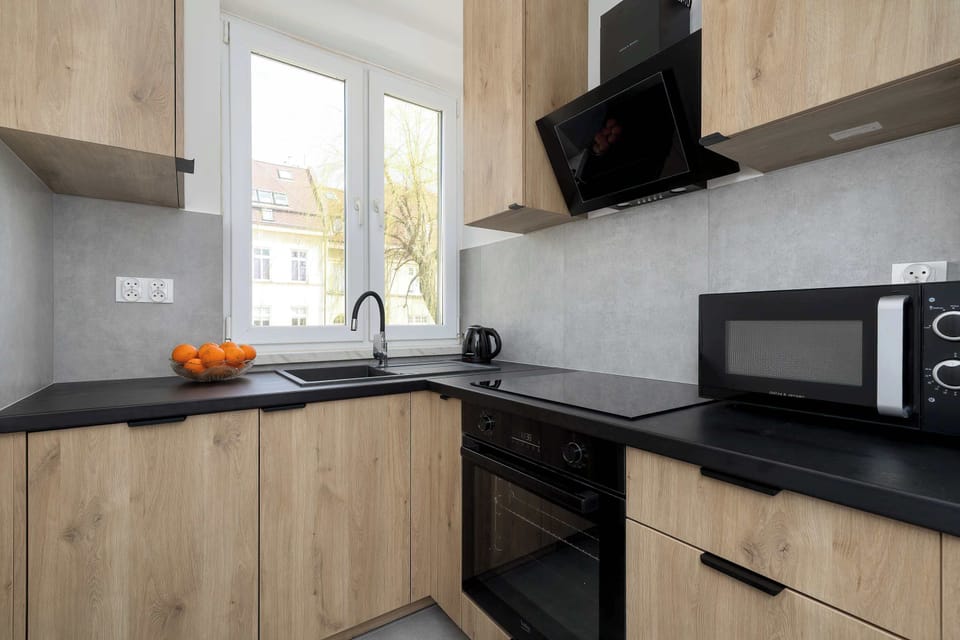 The kitchen workspace highlights a black countertop paired with light wood cabinetry and a built-in microwave. Natural light streams in from a window above the sink, illuminating the minimalist design.