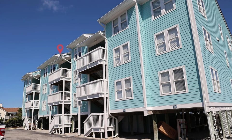 Charming turquoise beach house with multiple balconies and elevated design, offering coastal comfort under clear blue skies.