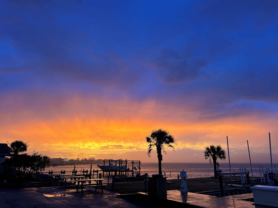 Stunning sunset paints the sky in vibrant oranges and blues over the waterfront marina area.