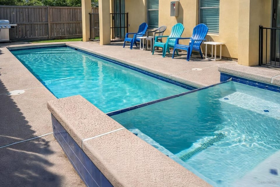 Sparkling pool & spa retreat with colorful seating, fenced privacy, and grill setup—perfect for sun-soaked relaxation and backyard vibes.