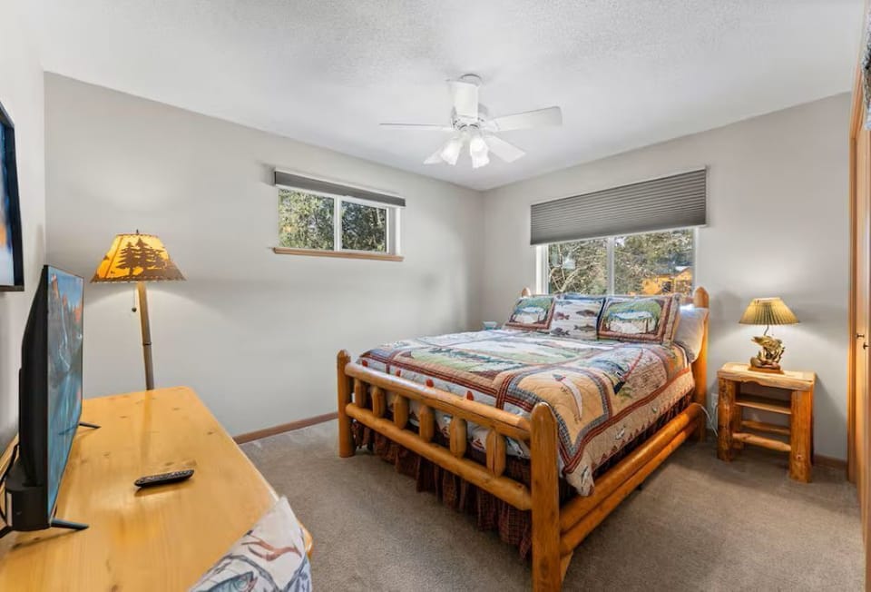 Cozy rustic bedroom with log bed, ceiling fan, TV, and treetop views