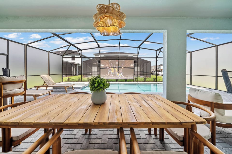 Savor your meals at the elegant wooden table, basking in natural light from the large screened doors that overlook the refreshing pool nearby. The warm tones and inviting decor set a perfect atmosphere for relaxation.