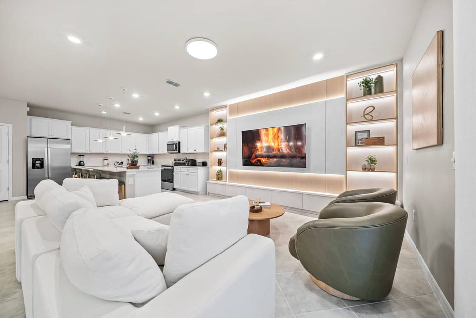 Relax in our spacious living area with a cozy white sectional and stylish green accent chairs. The warm lighting and modern decor, complemented by an electric fireplace, create a charming atmosphere perfect for unwinding.