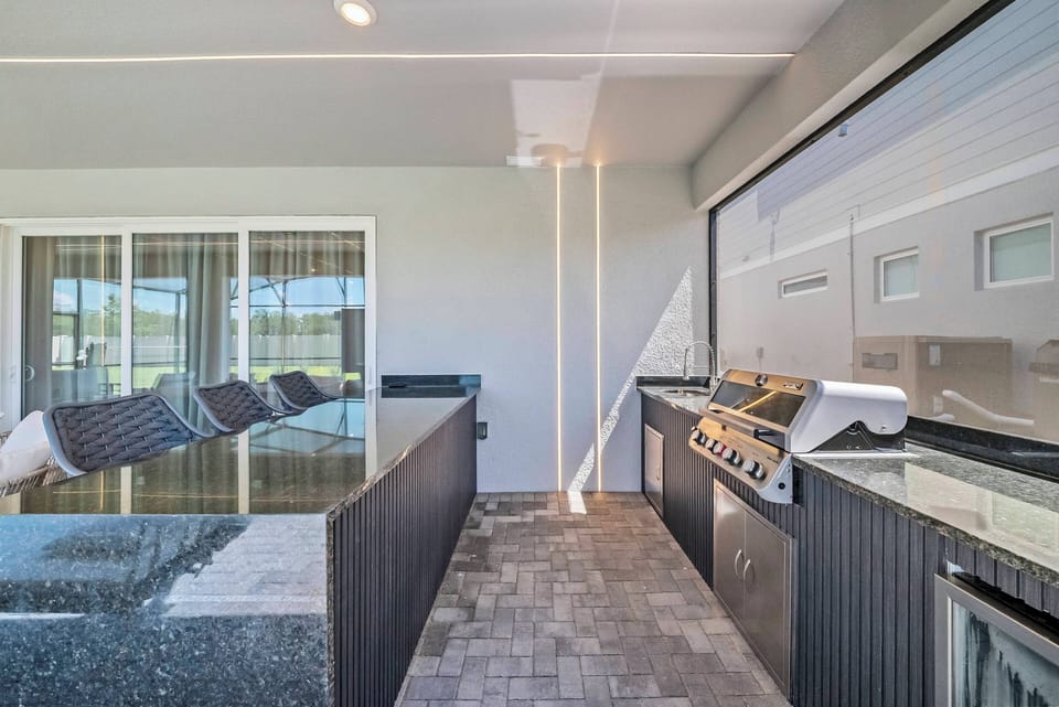 Step outside to this stylish outdoor kitchen, featuring a sleek black countertop and modern grill, perfect for al fresco dining. Relax on the adjacent lounge area, where soft cushions invite you to unwind and enjoy the view.