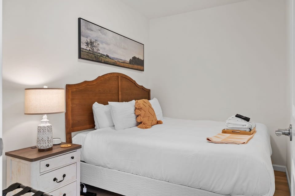 Bedroom with landscape artwork above the bed and a bedside lamp.