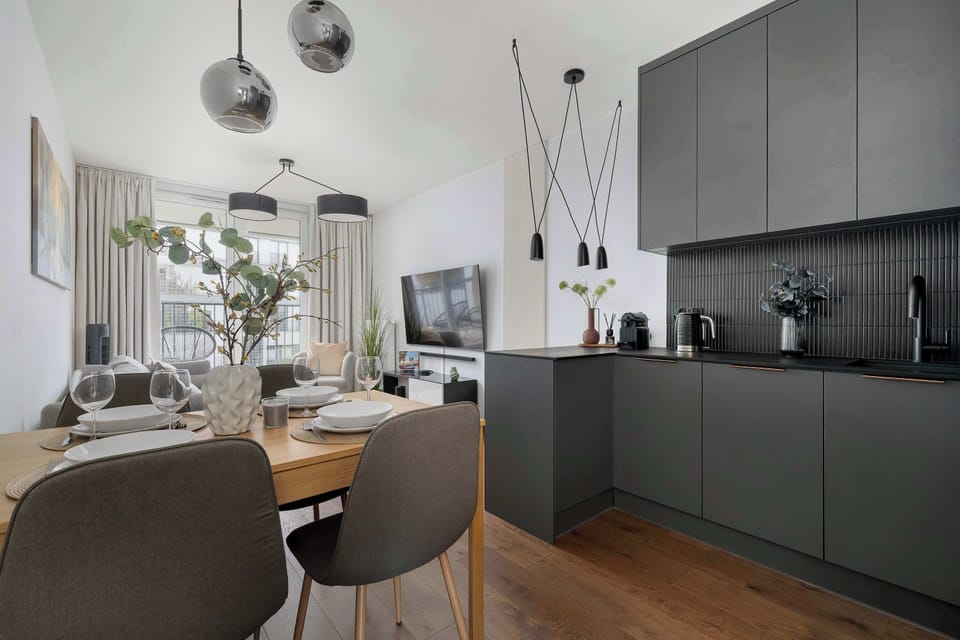 A modern kitchenette connected with a dining space, featuring sleek dark cabinets and wooden flooring. A dining table sits nearby, perfect for shared meals.