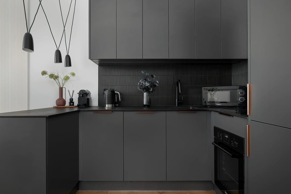 A stylish kitchenette with matte dark cabinetry and integrated appliances. Clean lines and minimalistic design give it a contemporary feel.