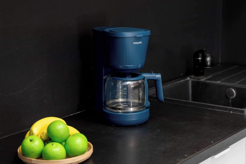 A close-up of a coffee machine on a countertop next to a bowl of green apples.