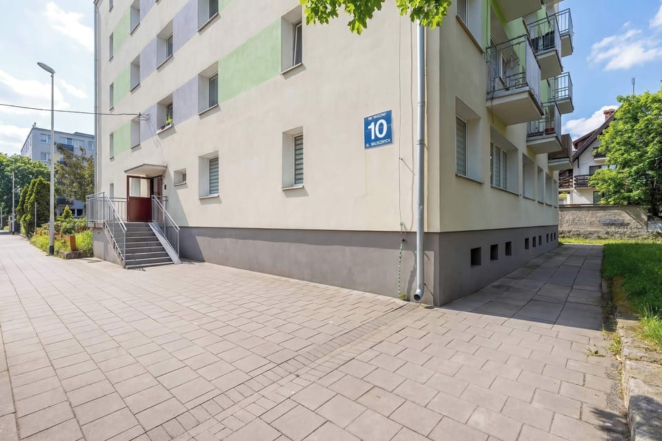 The exterior corner of a residential building with a sidewalk and greenery nearby.