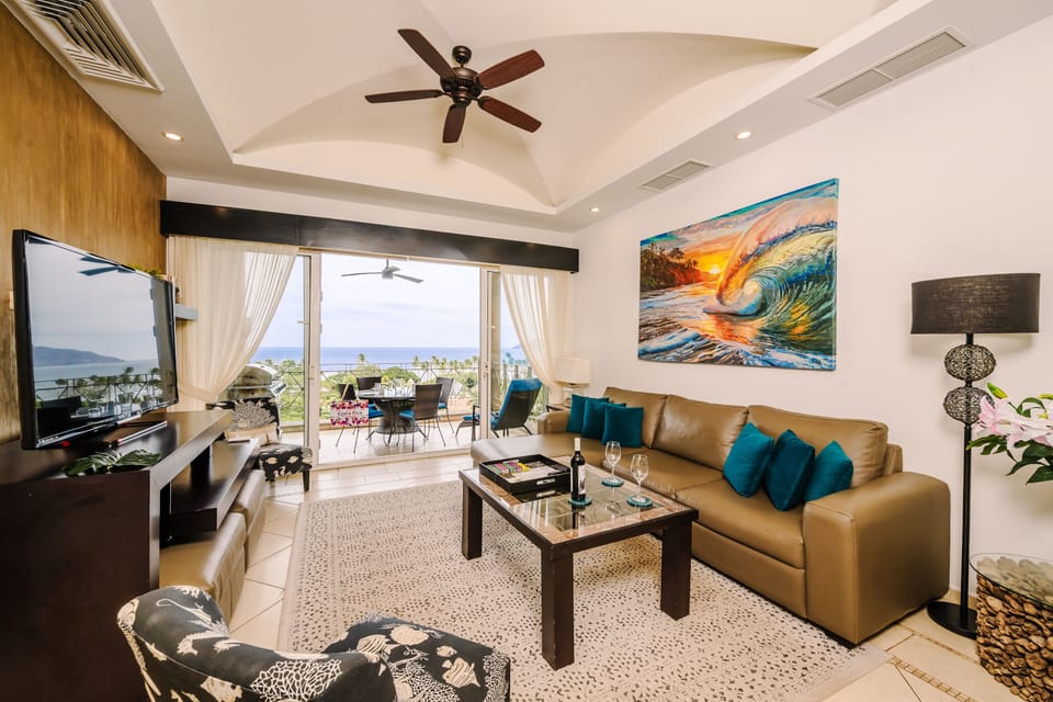 Open-concept living and dining with leather sectional, ocean-view sliders, and covered balcony with dining beyond.