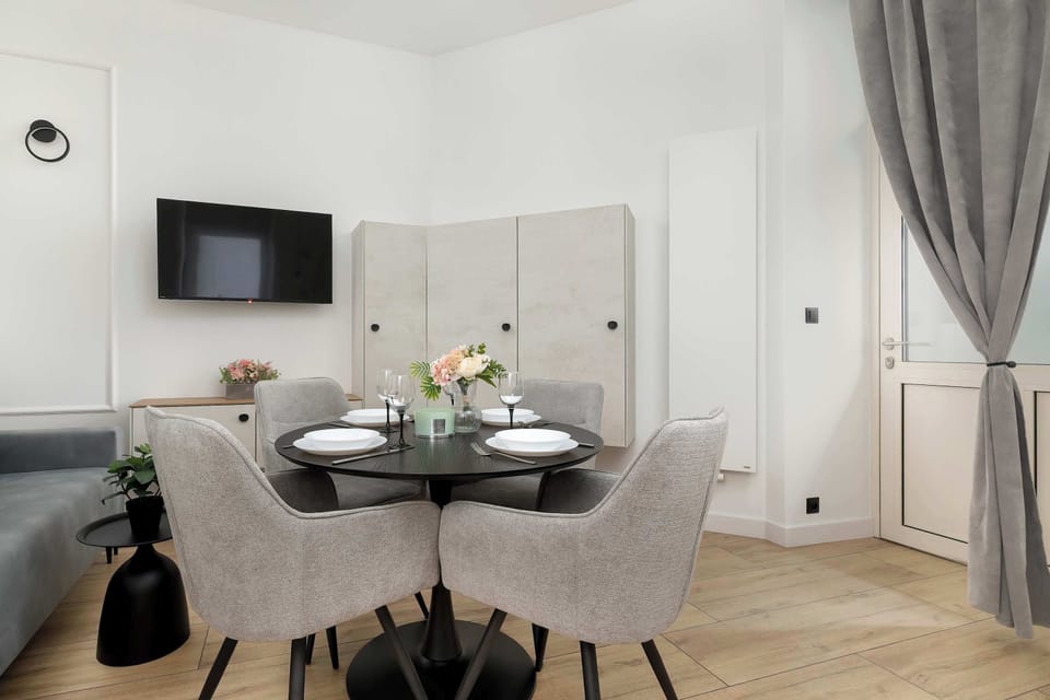A view of the living area, where a black table with flowers serves as the focal point, surrounded by elegant chairs and light-colored kitchen cabinets in the background.