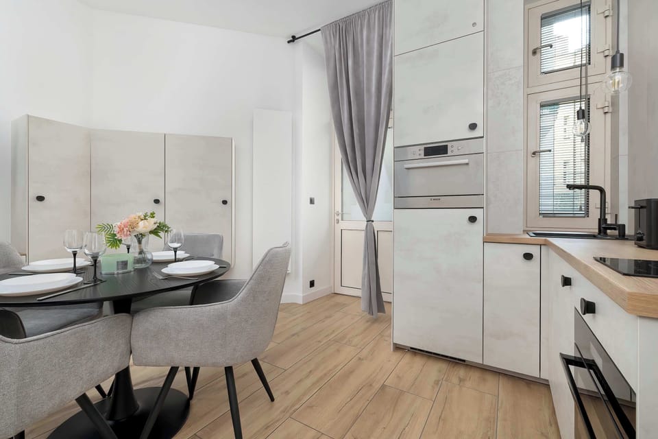 A close-up of the dining area, where the black, glossy tabletop contrasts with the light, soft upholstery of the chairs and the kitchenette.